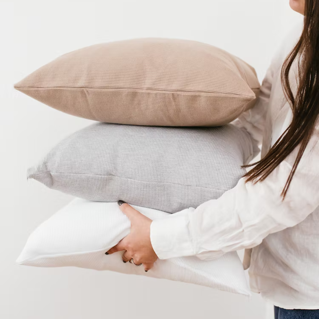  כריות נוי וופל מכותנה אורגנית מסודרות בשורה, ומציגות את צבעי הקולקציה: לבן שלג, אפור מלאנג' וחום שוקו.